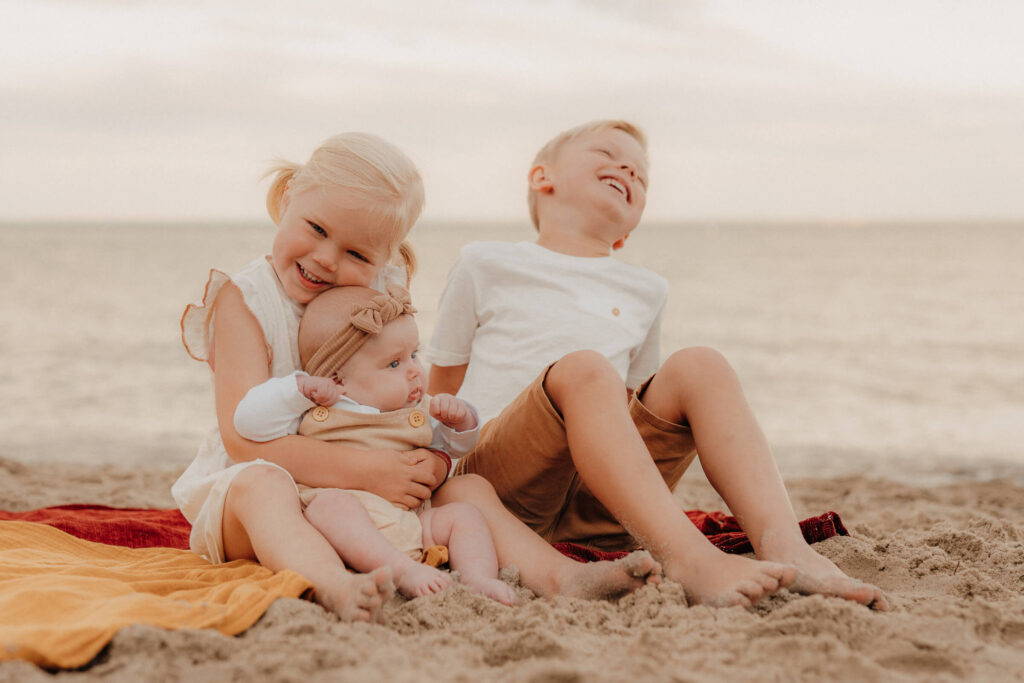 familienshooting ostsee strand, drei kinder sitzen zusammen und lachen