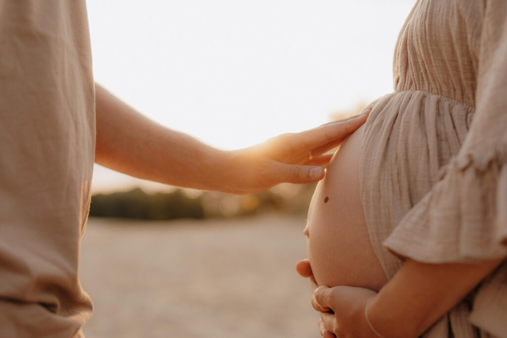 babybauchshooting boberger duenen, partner beruehrt babybauch seiner schwangeren frau im sonnenuntergang golden hour