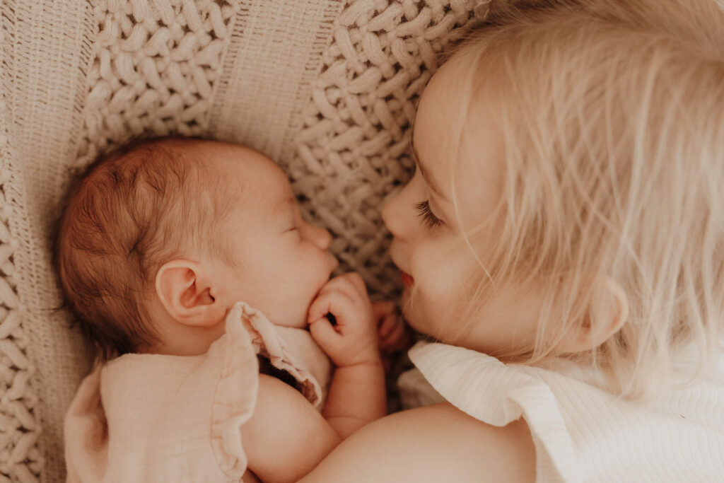 newbornshooting, baby und grosse schwester liegen auf einer decke und gucken sich an