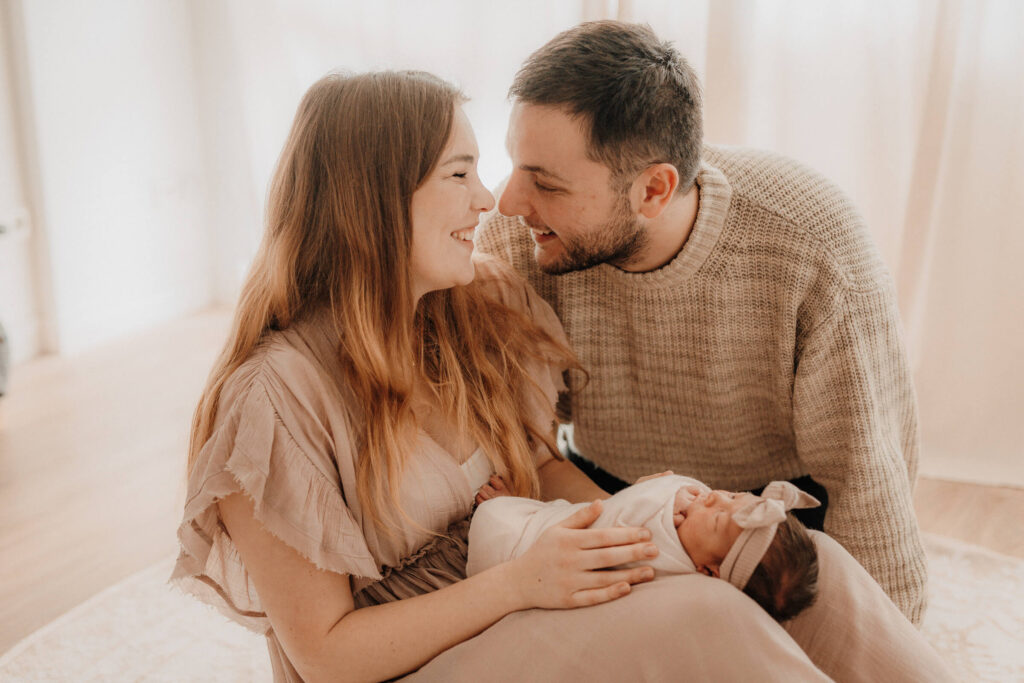 newbornshooting homeshooting, baby liegt auf mamas beinen, mama und papa lachen sich an