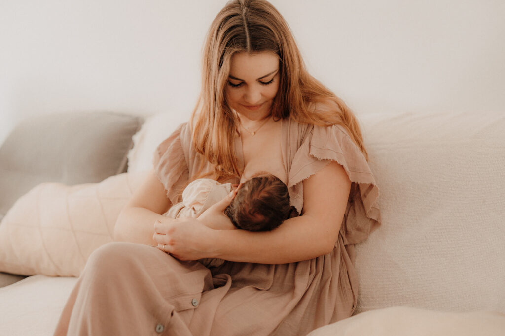 newbornshooting, mama und baby sitzen auf dem sofa, baby wird gestillt