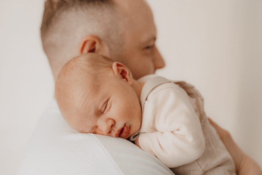 newbornshooting, baby liegt und schlaeft auf papas schulter