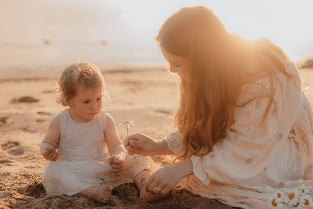 mama kind shooting, sitzen am strand und spielen im sand im sonnenuntergang
