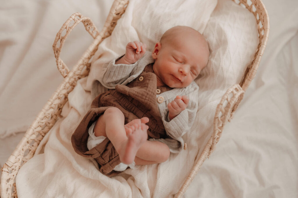 newbornshooting, baby liegt im korb und schlaeft, ueberkreuzt die beine