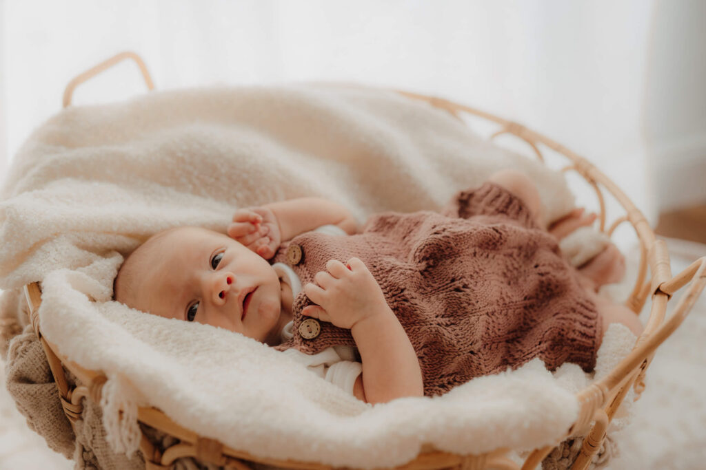 newbornshooting, baby liegt im korb und guckt zufrieden