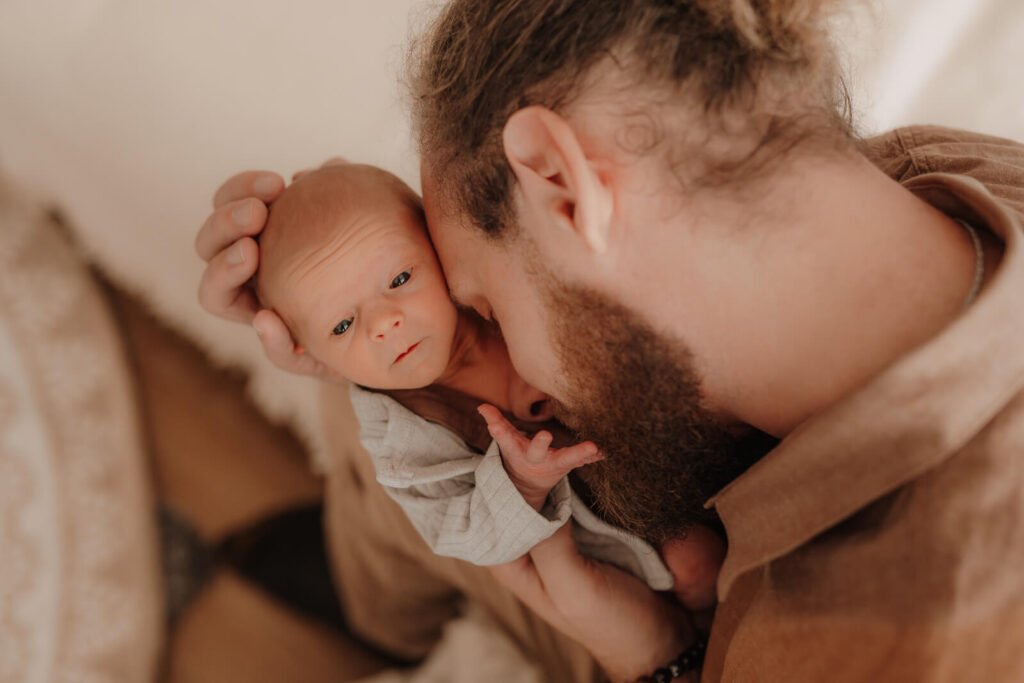 newbornshooting, baby liegt in papas arm und er schmiegt sich an