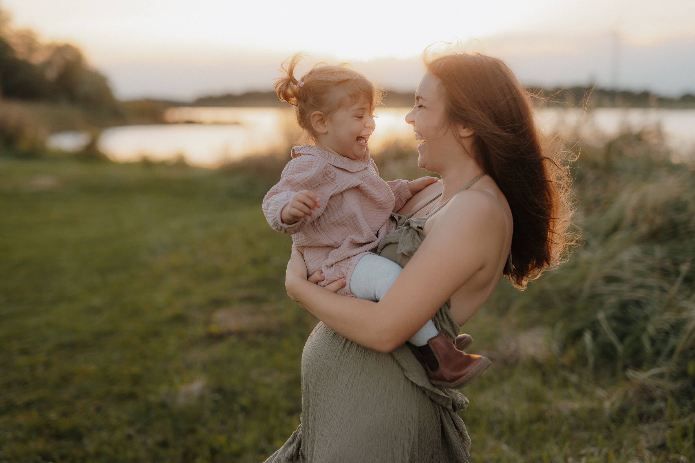 babybauchshooting, mama mit grosser schwester auf dem arm, lachen sich an